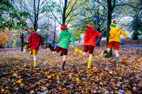 Four people in colourful autumn clothes dance in autumn leaves