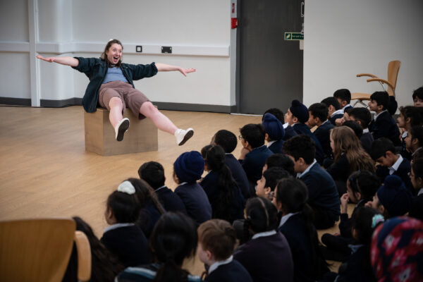 In front of an audiences of children a person sit's on a box, pretending to fly