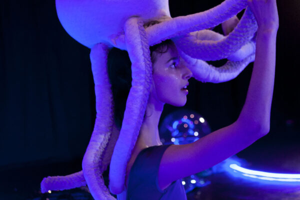 A performer dances with a stuffed octopus on their head